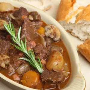 White Plate Filled with Beef Bourguignon Next to a Bread