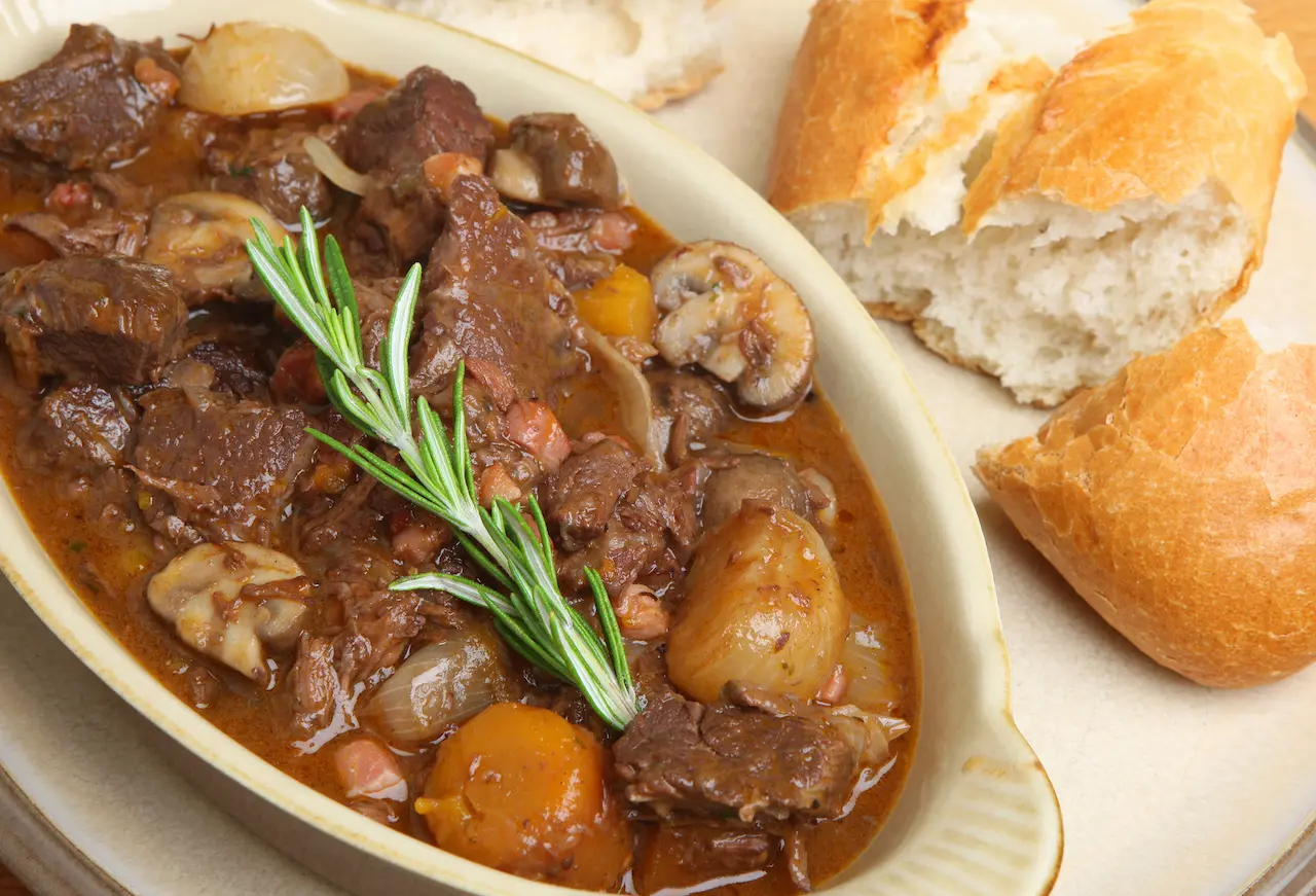 White Plate Filled with Beef Bourguignon Next to a Bread