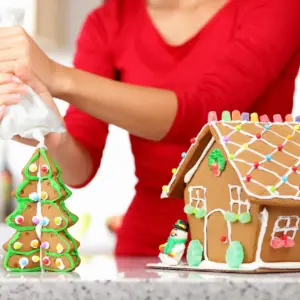 Woman Decorating Gingerbread House With Whip Cream