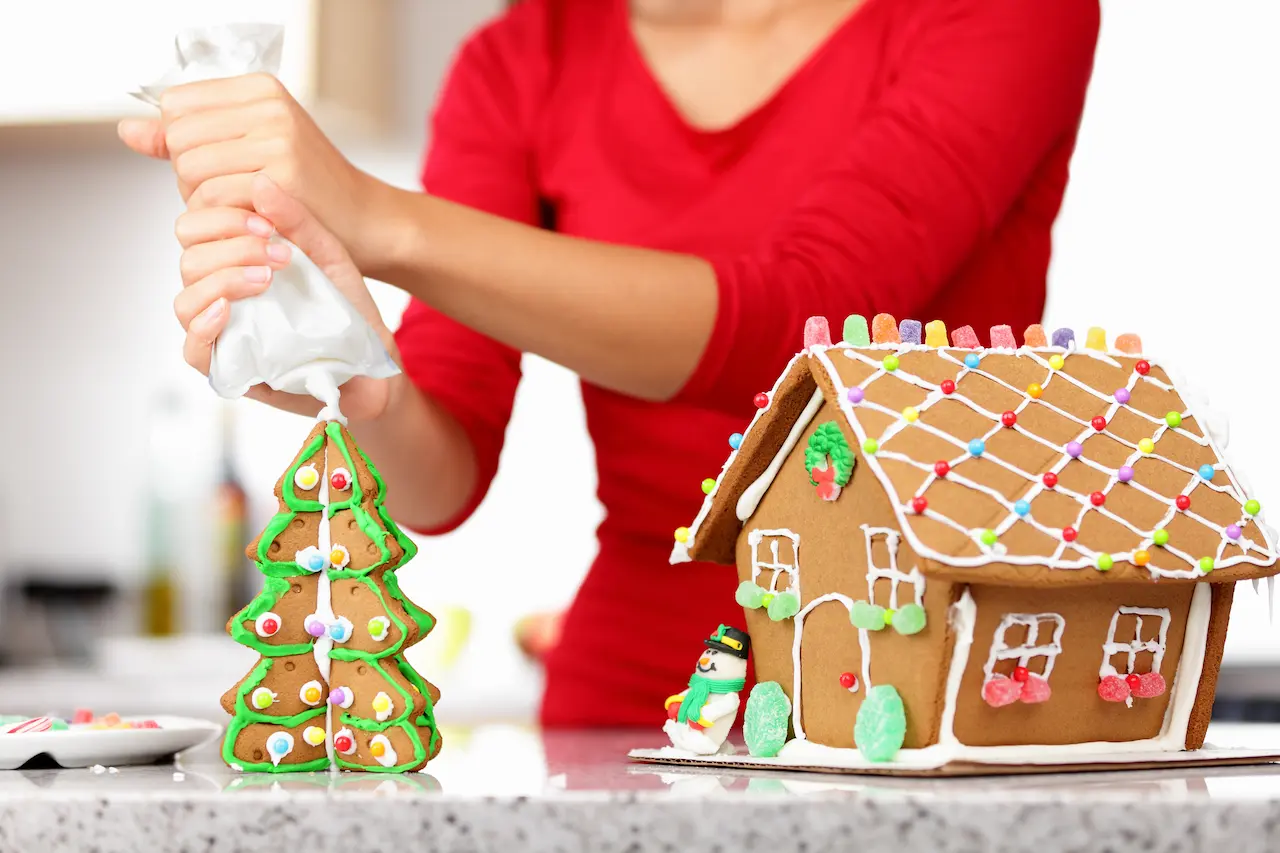 Woman Decorating Gingerbread House With Whip Cream