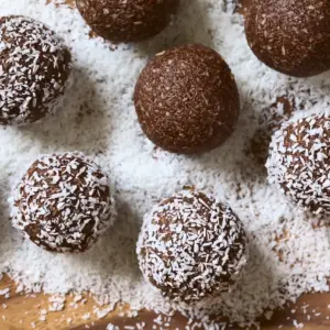 Rum Balls Being Covered with Grated Coconut on Wooden Plate