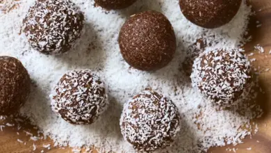 Rum Balls Being Covered with Grated Coconut on Wooden Plate