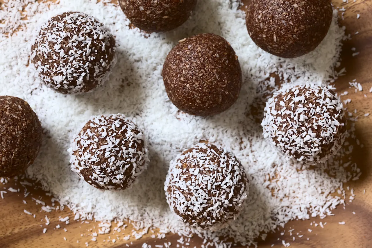 Rum Balls Being Covered with Grated Coconut on Wooden Plate