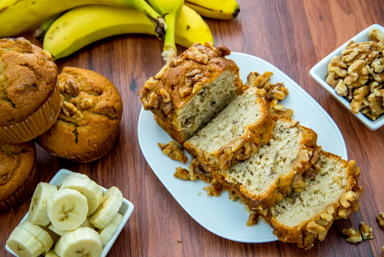 Uber-moist Banana Bread on a White Plate Next to Fresh Banana Cupcake